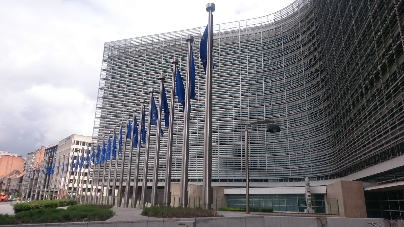 Flagi Unii Europejskiej przed budynkiem Berlaymont w Brukseli, siedzibą Komisji Europejskiej, która 19 października 2026 roku opublikowała odniesienie do pierwszej normy zharmonizowanej dla AI Act